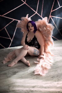 Woman with purple hair wearing pink angel wings sitting on the ground