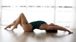 A woman in a boudoir pose on the floor with light coming in the window. 