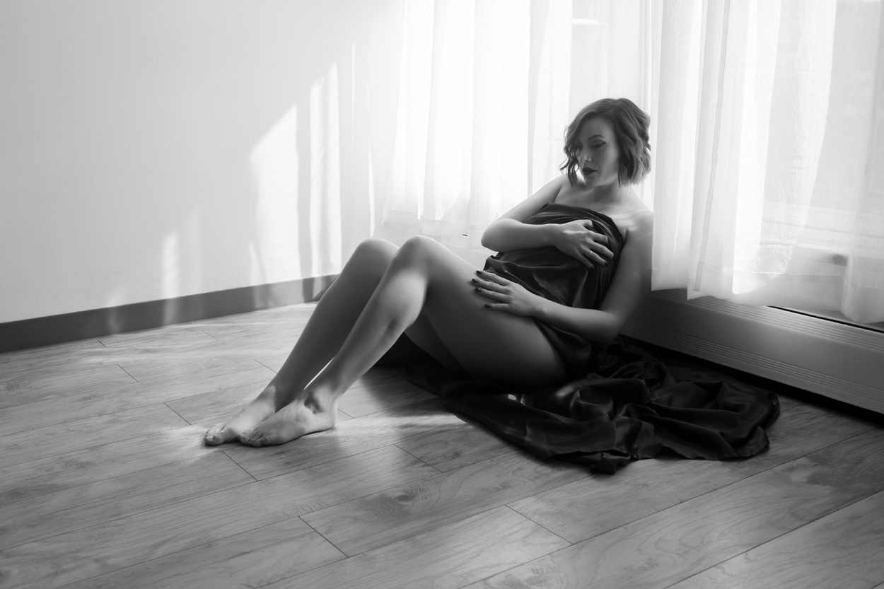 Boudoir Image of a beautiful women lying in front of a bright window, covered in just a sheet.