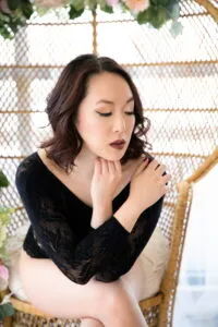 Woman with brown hair wearing black bodysuit, sitting in a peacock chair