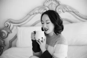 Woman relaxes in bedroom with a coffee cup and a sweater